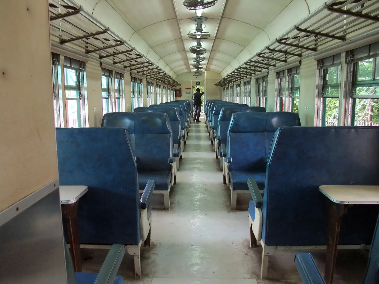 Blue upholstered seats, central aisle, windows and luggage racks inside a historical coach